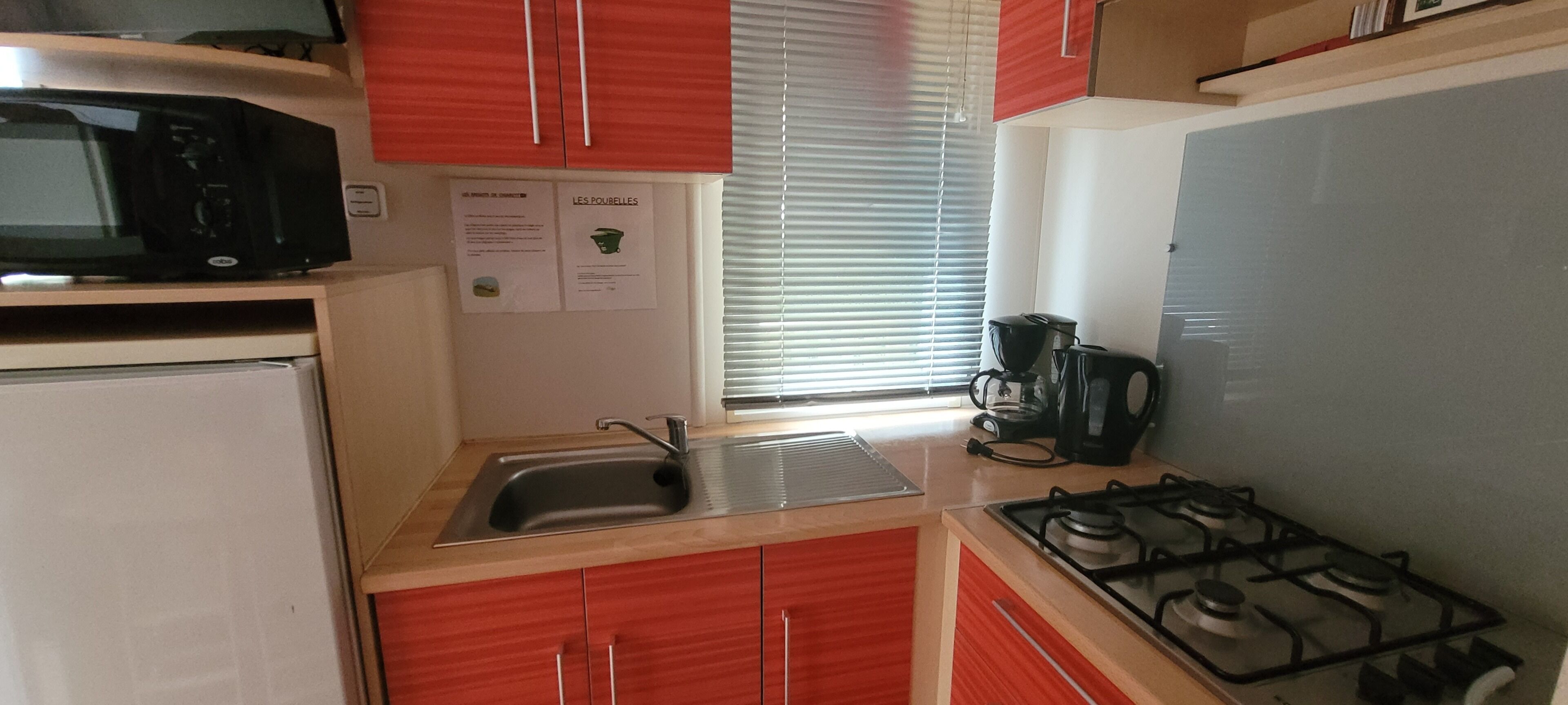 Une cuisine de taille réduite, équipée d’un évier, d’une cuisinière, d’un four à micro-ondes et de placards rouges.
