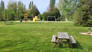 Un parc équipé d’une table de pique-nique, d’aires de jeux et d’arbres.