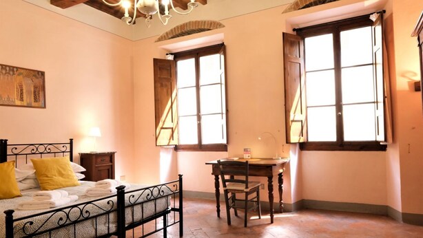 Une chambre à coucher comprenant un lit, une table de chevet, une lampe, un bureau, une chaise et deux fenêtres.