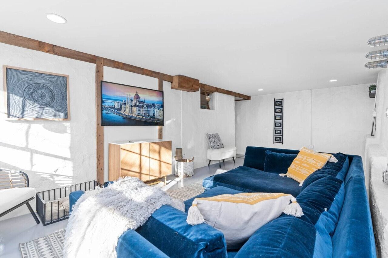 A modern living room with a blue sofa set, a white armchair, and a large flat-screen TV mounted on the wall.