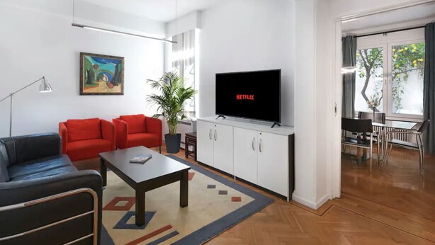 Een moderne woonkamer met een flatscreentelevisie, rode banken, een salontafel en een eetgedeelte met een tafel en stoelen.