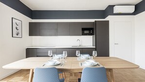 Une cuisine moderne avec des meubles de couleur sombre, un four à micro-ondes et un coin repas doté d’une table en bois, mise pour quatre personnes.