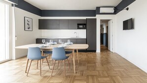 Une cuisine moderne dotée d’un îlot central, de meubles de rangement aux couleurs sombres et d’un coin repas avec des chaises bleues.