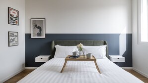Une chambre à coucher bien rangée, avec un lit, des tables de chevet, un plateau avec des tasses et des œuvres d’art encadrées accrochées au mur.