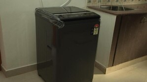 A compact black refrigerator in a kitchen with a tiled floor and a wooden cabinet. - Izi Apollo Stay (Chennai)
