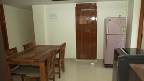 A small, clean room with a wooden dining table and chairs, a wooden wardrobe, and a pink refrigerator. - Izi Apollo Stay (Chennai)