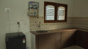 A compact kitchen with a sink, a refrigerator, and a window with bars. - Izi Apollo Stay (Chennai)