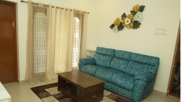 A living room with a blue sofa, a wooden coffee table, and a patterned rug. - Izi Apollo Stay (Chennai)