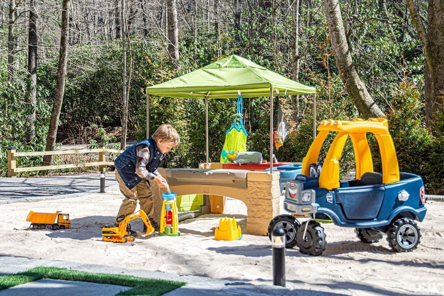 A child playing with toy vehicles and a sandbox in an outdoor play area.