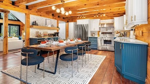 A modern kitchen with wooden beams, a dining area with a large table and bar stools, and a blue accent wall.