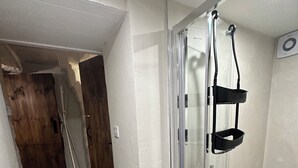 Une douche fermée par des parois de verre, avec une structure en métal, un plancher en bois et un mur blanc.