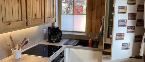 A modern kitchen with wooden cabinets, a black coffee maker, a sink, and a refrigerator with magnets.