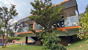 Una casa moderna de dos pisos con balcón, rodeada de vegetación y una piscina.