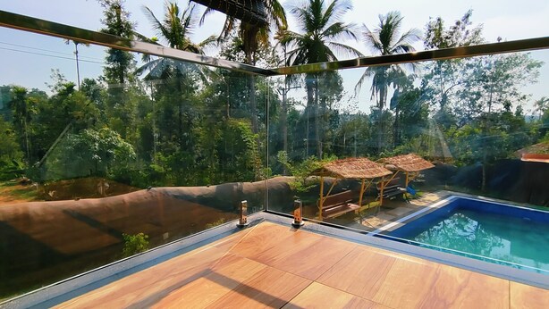 Un área de piscina con paredes de vidrio, un muelle de madera, rodeada de abundante follaje y palmeras.