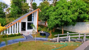 Una casa moderna con techo inclinado, amplios ventanales y un jardín cuidado con cerca y fuente de agua.