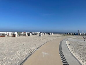 En sandstrand med vita byggnader, en svängd gångväg och en klarblå himmel.