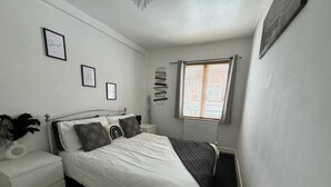A bedroom with a bed, bedside tables, a window with blinds, and wall decorations. - Cosy 3-bed Apartment in Hythe High Street (Hythe)