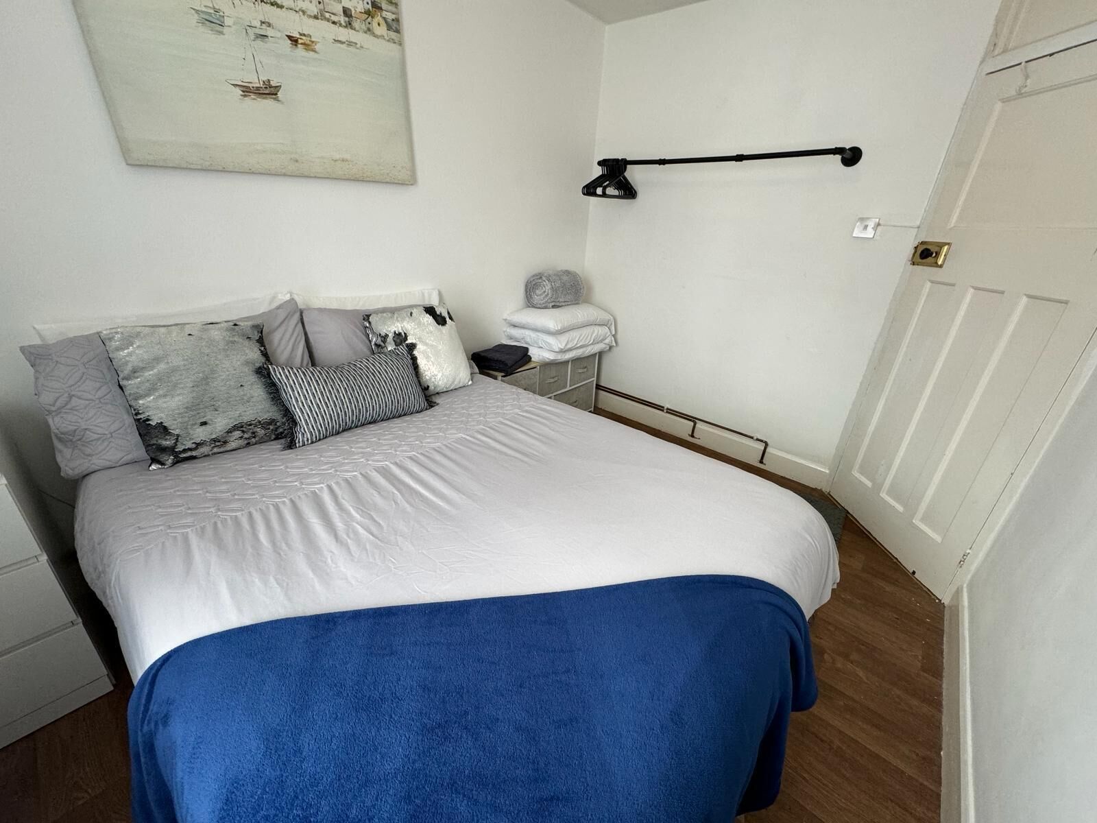 Una camera da letto con un letto, cuscini, un comodino, una lampada e un quadro appeso al muro.