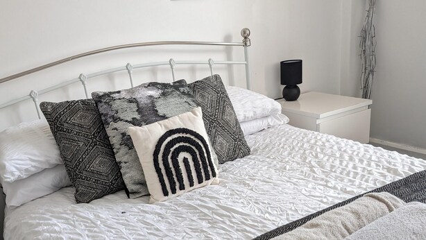 A neatly made bed with a white duvet, black and white patterned pillows, and a black and white herringbone throw blanket. - Cosy 3-bed Apartment in Hythe High Street (Hythe)