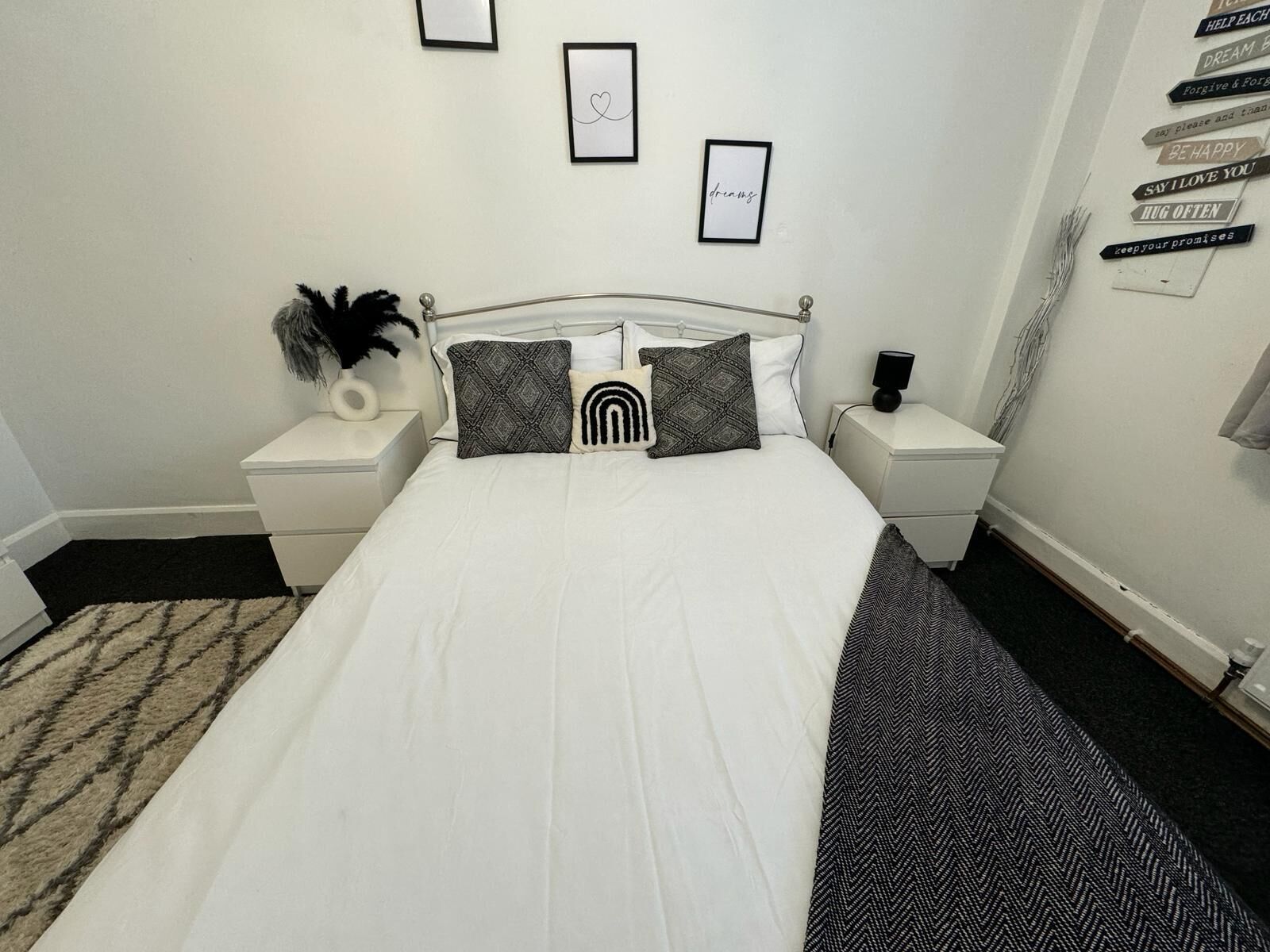 Una camera da letto ben ordinata con un letto grande, due comodini, una mensola a parete e una citazione motivazionale incorniciata.