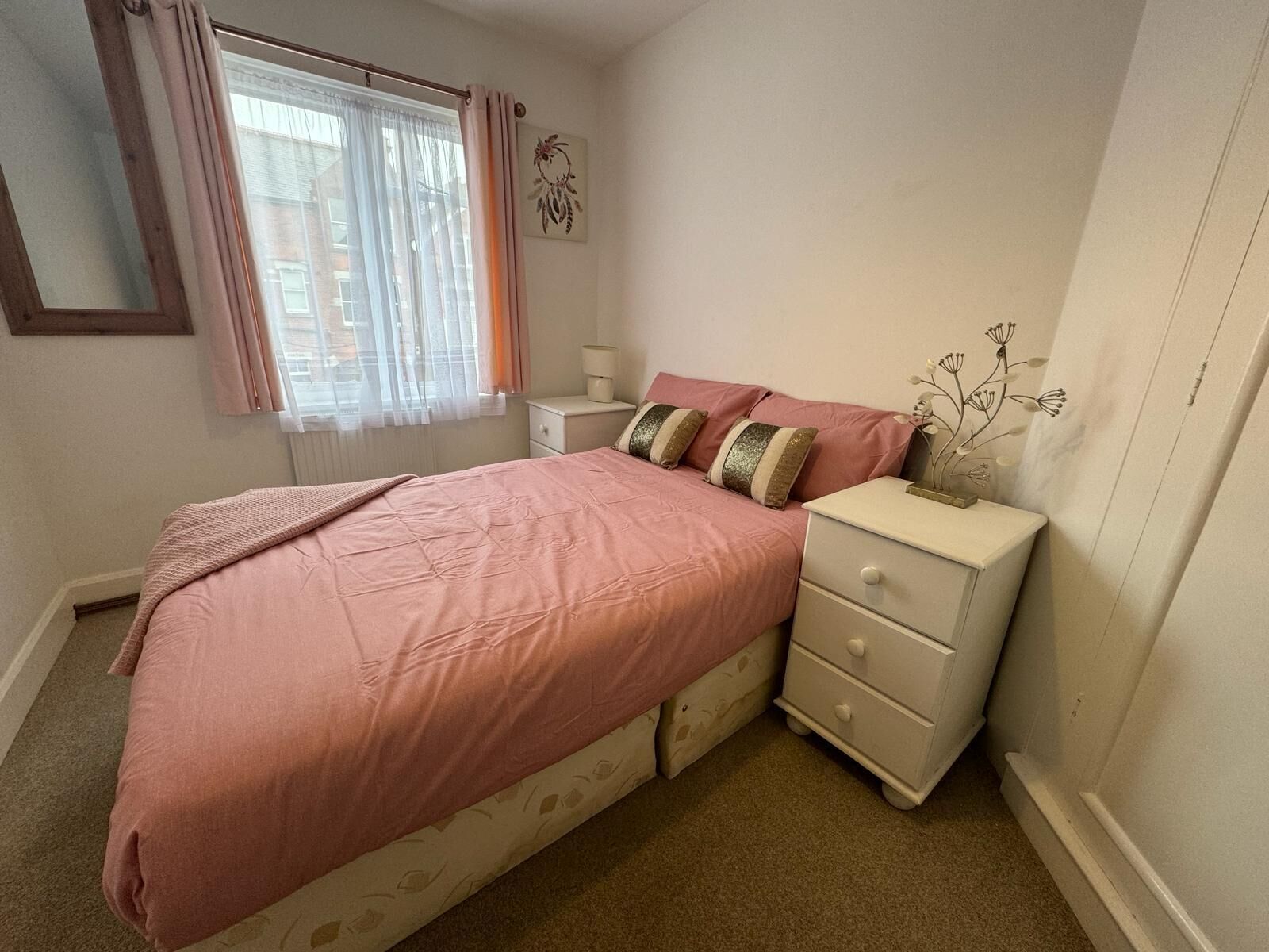 A bedroom with a bed, a bedside table, a nightstand, and a window with curtains.