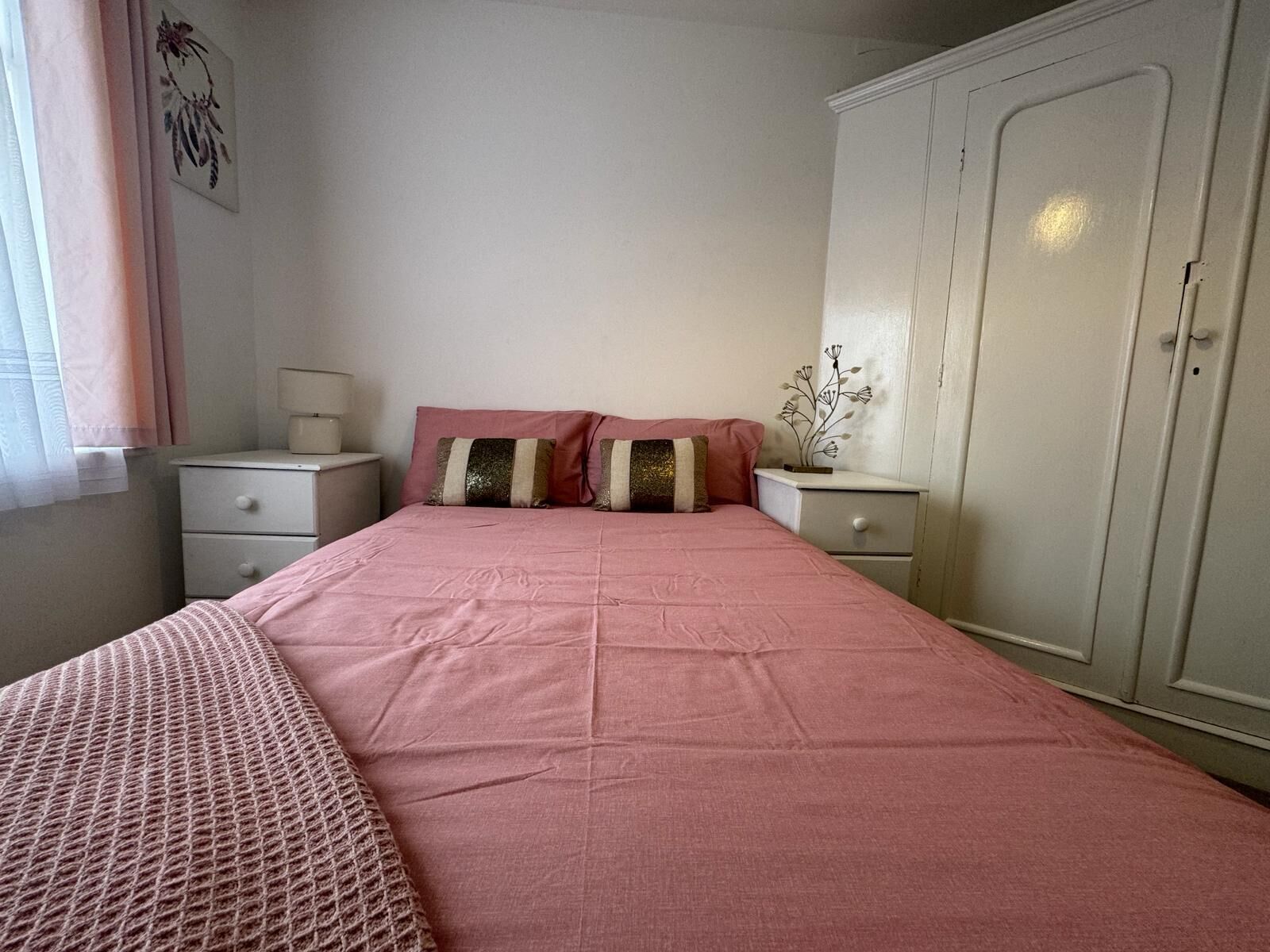 A bedroom with a single bed, two bedside tables, a wardrobe, and a window with curtains.