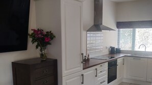 A modern kitchen with white cabinets, a black range hood, and a window with blinds. - Gateway to Killarney (Killarney)