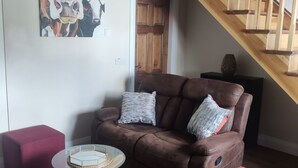 A living room with a brown leather sofa, a glass coffee table, a red ottoman, and a wooden staircase. - Gateway to Killarney (Killarney)