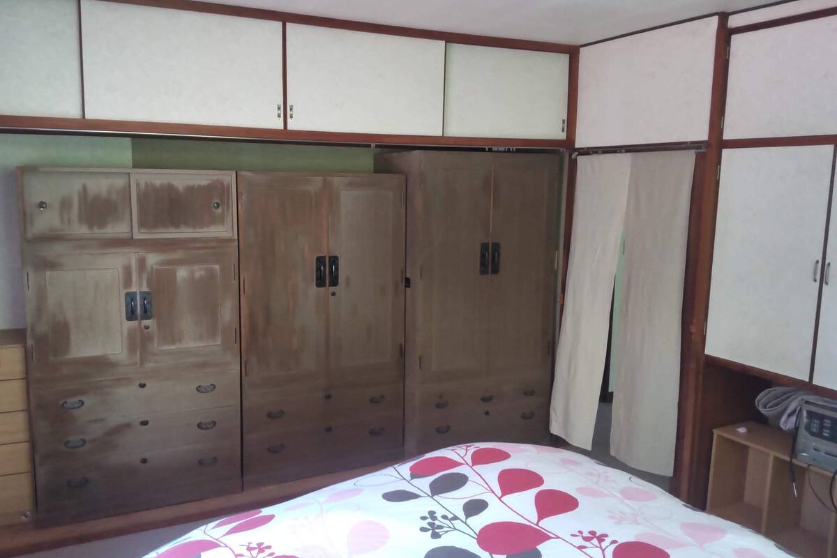 Quarto com cama, guarda-roupa de madeira e uma pequena mesa com micro-ondas.