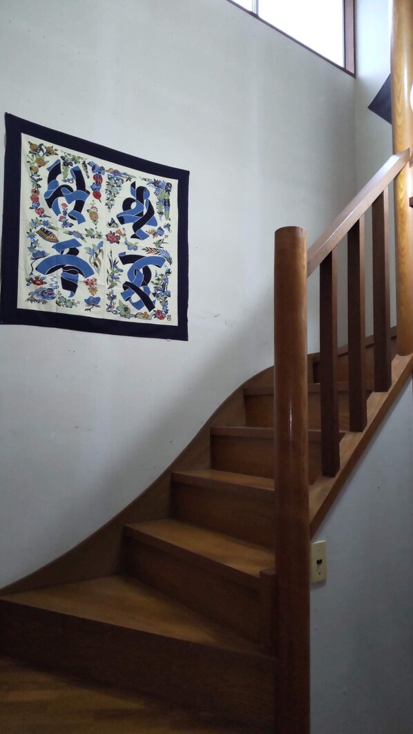 Una escalera de madera con barandilla, que lleva a un rellano con una obra de arte enmarcada con diseños abstractos y motivos florales.