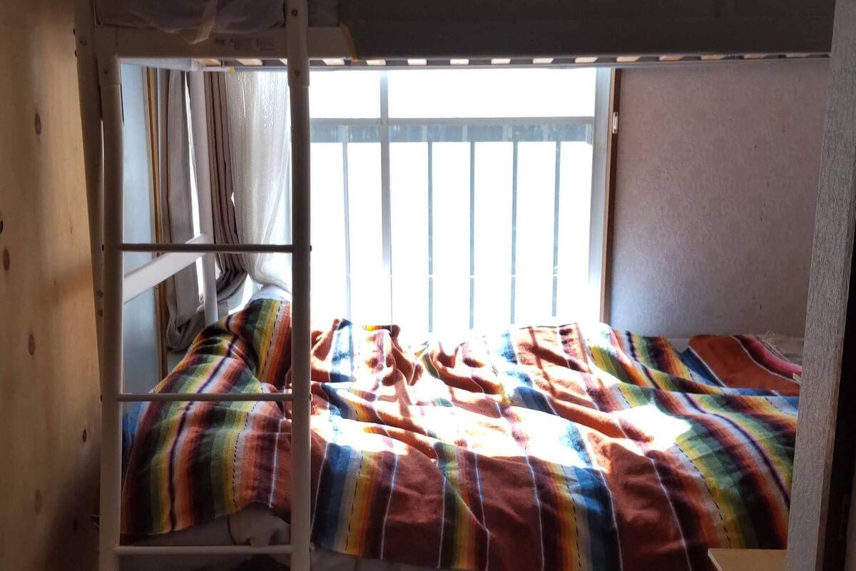 Quarto com beliche, janela, cortinas e um cobertor colorido.