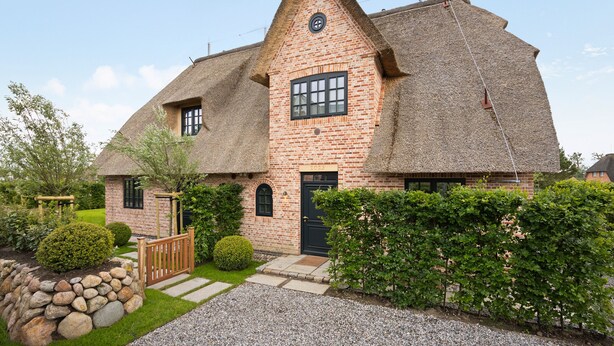 A brick house with a thatched roof, a small garden, and a gravel driveway. - Neubau. Wellness. Reet (List auf Sylt)