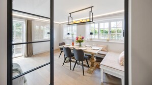 A bright dining area with a large table, chairs, and a hanging light fixture. - Neubau. Wellness. Reet (List auf Sylt)