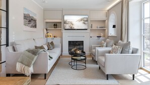 A modern living room with a fireplace, a flat-screen TV, and a large window. - Neubau. Wellness. Reet (List auf Sylt)
