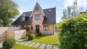 Une maison à deux étages, dotée d’un toit à forte pente, d’une façade en briques et d’une pelouse bien entretenue agrémentée de chemins en pierre.