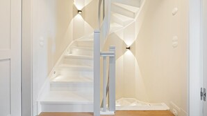 Un escalier blanc avec une rampe centrale et des luminaires fixés au mur.