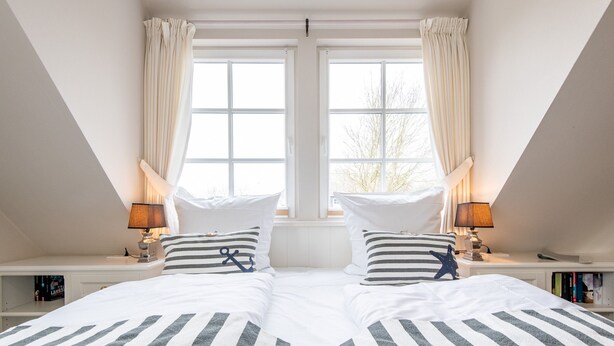 A bedroom with two beds, white bedding, striped pillows, and a starfish decoration. There are bedside tables with lamps and bookshelves. - Gemütlich. Ruhig. Garten (Sylt)