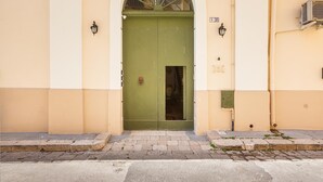 Una puerta verde con una pequeña ventana, una placa de número y un equipo de aire acondicionado fijado a la pared.
