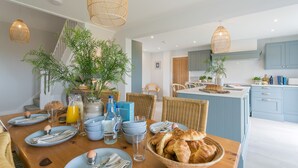 Una cocina moderna con armarios azules, un comedor con sillas de mimbre y un desayuno con cruasanes y huevos.