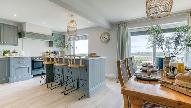 Una cocina moderna con una isla central, taburetes de bar y una mesa de comedor preparada para seis comensales.