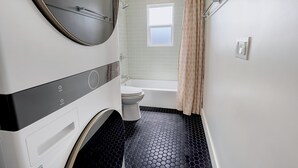 A compact bathroom with a toilet, a washing machine, and a shower area. - 2 Bedroom Craftsman:KING Bed:Office:Views:Parking::Between Disney/Universal (Whittier)