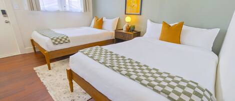 Ein Hotelzimmer mit zwei Einzelbetten, einem Nachttisch mit Lampe, einem gerahmten Kunstwerk an der Wand und Holzboden.