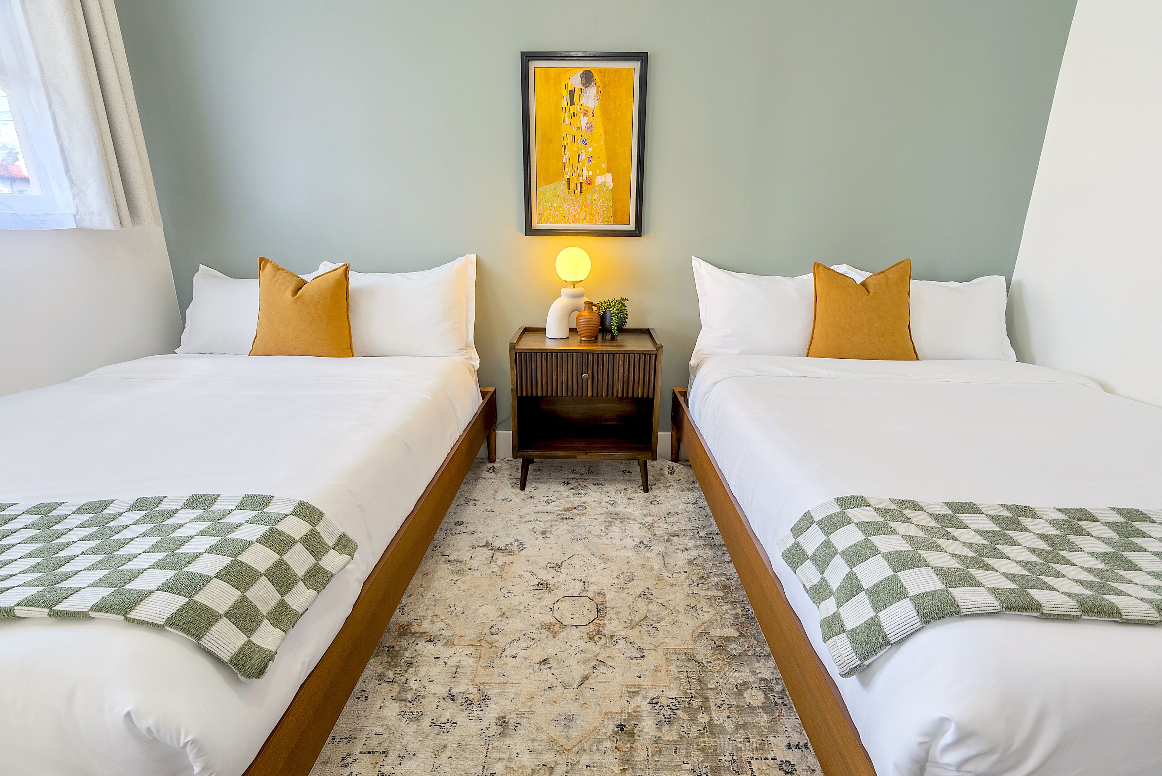 Habitación de hotel con dos camas, una mesita de noche con lámpara y un cuadro en la pared.