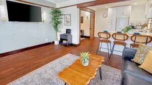 A modern living room with a wooden coffee table, a TV mounted on the wall, and a dining area with chairs and a table. - 2 Bedroom Craftsman:KING Bed:Office:Views:Parking::Between Disney/Universal (Whittier)