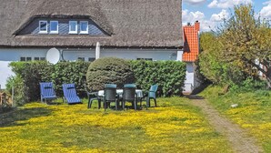 Una casa con tetto di paglia, antenna parabolica e giardino con fiori gialli e mobili da esterno.