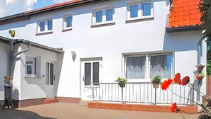 Un edificio bianco con tetto rosso, numerose finestre e un piccolo balcone con piante in vaso.