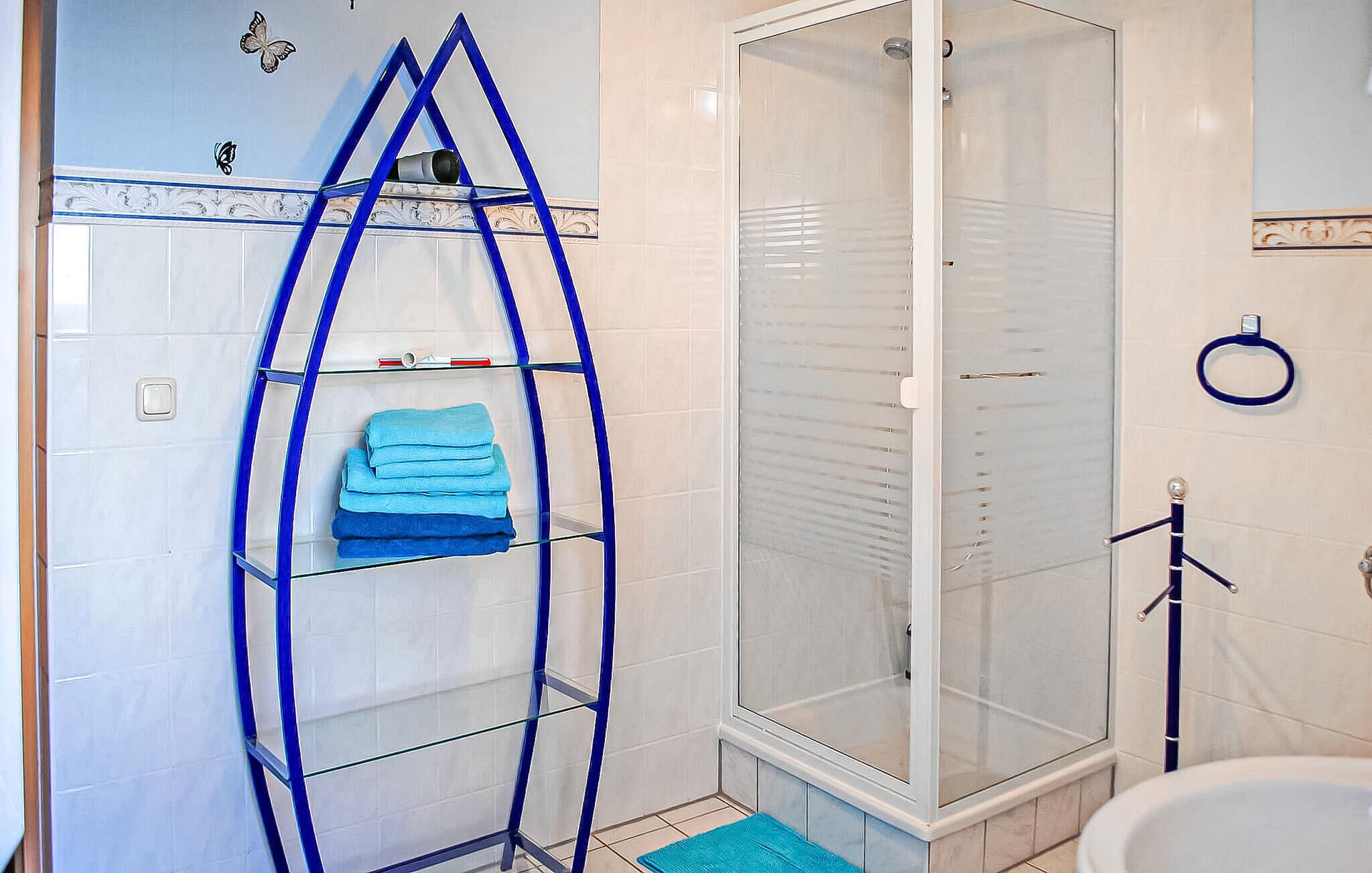 A bathroom with a glass shower enclosure, a blue towel rack, and a toilet.