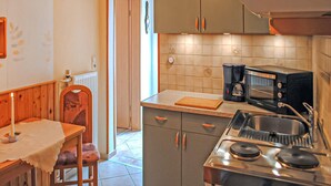 Una cucina funzionale con piano cottura, forno a microonde e macchina da caffè. Si vede una sedia di legno e un tavolo con tovaglia bianca.