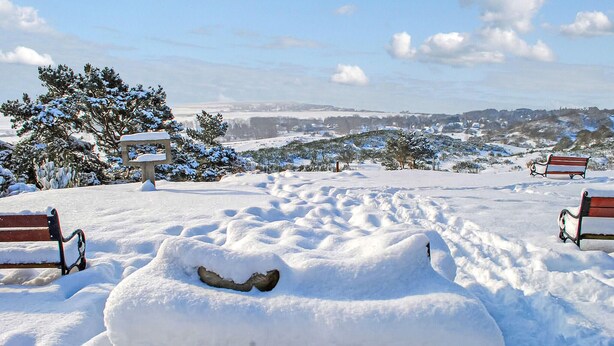 Un parco innevato con panchine e un muro in pietra.