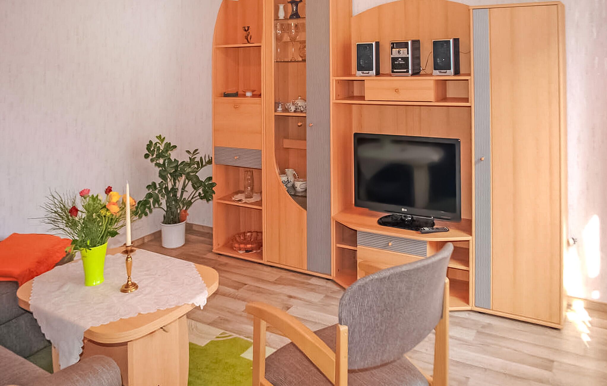 A compact living space with a TV, wooden furniture, a small table with a vase of flowers, and a potted plant.